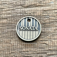 Load image into Gallery viewer, Personalised piano keys dog ID tag deeply engraved into brushed nickel silver metal with raised Sonata name and vertical keyboard pattern on rustic wood background