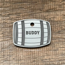 Load image into Gallery viewer, hiskey Barrel shape Dog tag with 'Buddy' engraved on a wooden surface, branded 'The Barking Tagsmith'.