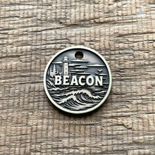 Load image into Gallery viewer, Personalised lighthouse dog ID tag with engraved ocean waves, coastal lighthouse and shoreline scene in brushed silver metal on rustic wood background
