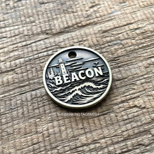 Load image into Gallery viewer, Personalised lighthouse dog ID tag with engraved ocean waves, coastal lighthouse and shoreline scene in brushed silver metal on rustic wood background