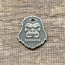 Load image into Gallery viewer, Dog ID tag shaped like a Sasquatch Bigfoot face with deep engraved details and the name Sasquatch, personalised engraved metal pet tag for cryptid fans.